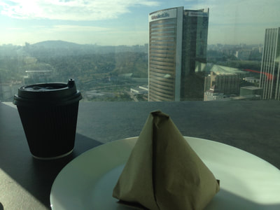 Blick aus dem Fenster im 28. Stock: Im Vordergrund ein Pappbecher mit Kaffee, daneben verpacktes Nasi Lemak, dahinter sieht man die Bürogebäude von Kuala Lumpur